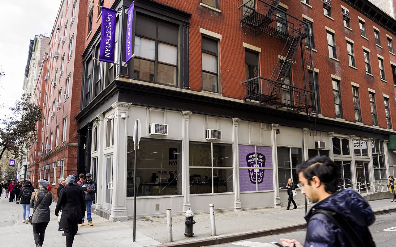 People walking by the NYU Public Safety Office located on Mercer Street. It has a large decal on the window featuring a badge and the words 