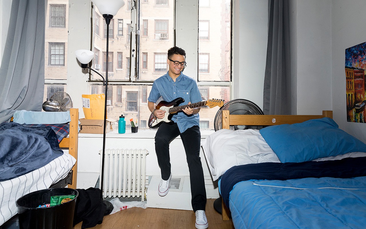 A student playing a guitar in his dorm room.