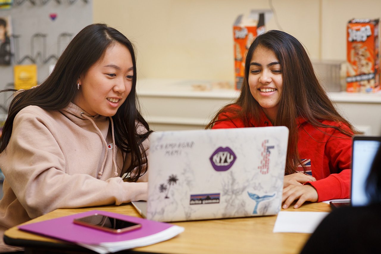 Two students of color working together on a laptop.