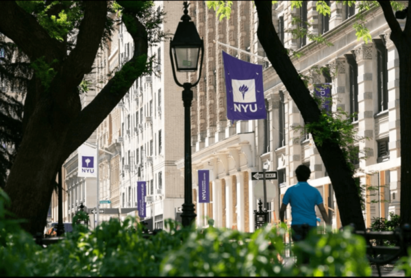 Student walking through campus with an NYU flag and building in the background.