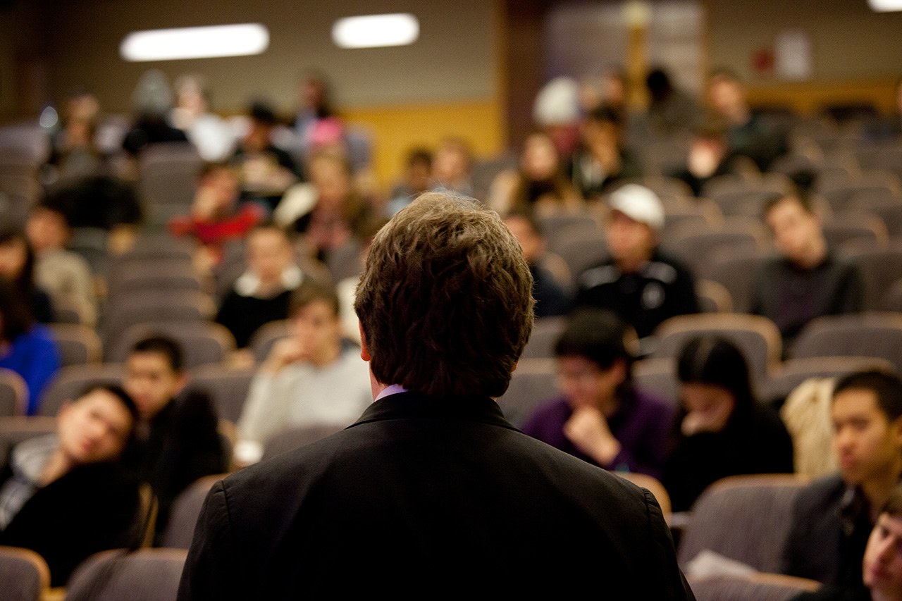 The back silhouette of a professor facing a lecture hall.