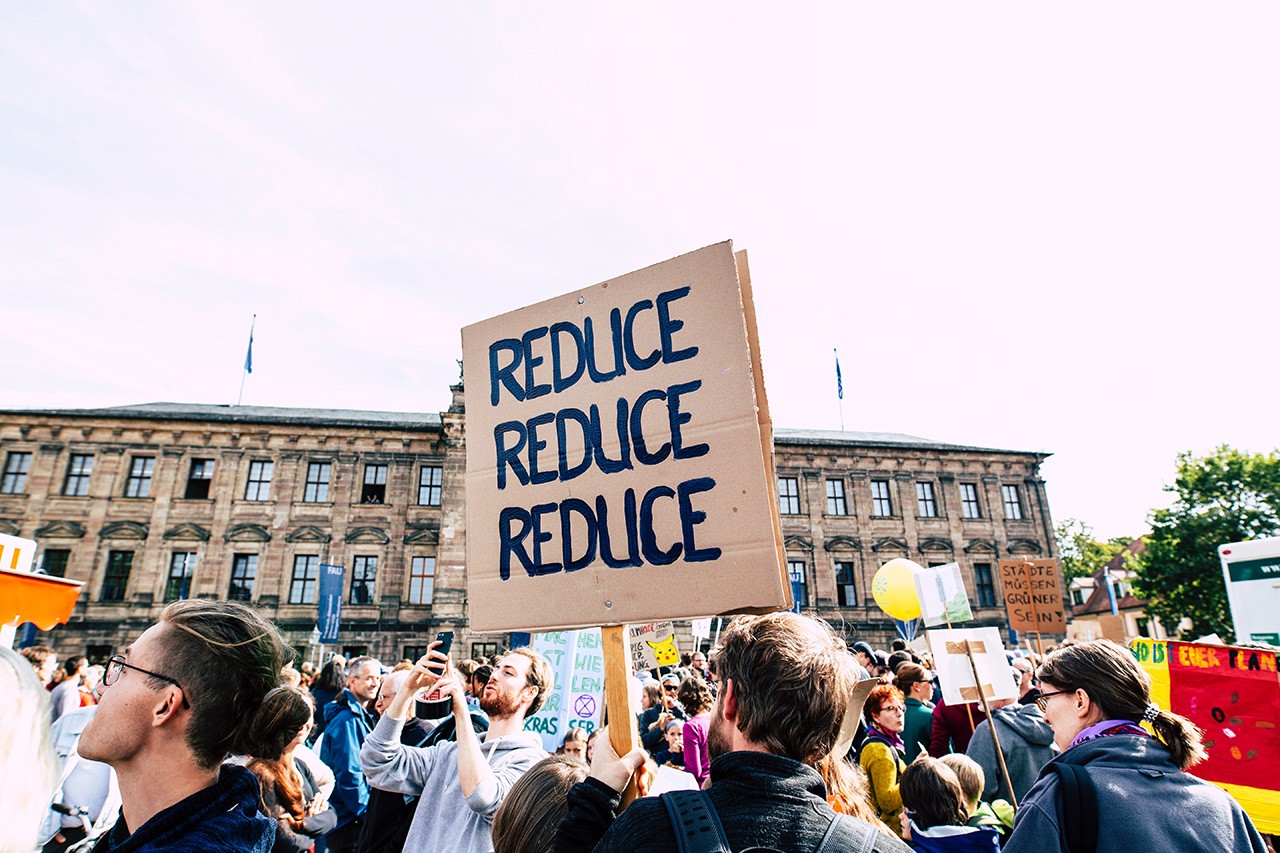 Protestor holding a sign, reading “Reduce, Reduce, Reduce,” to promote waste reduction.
