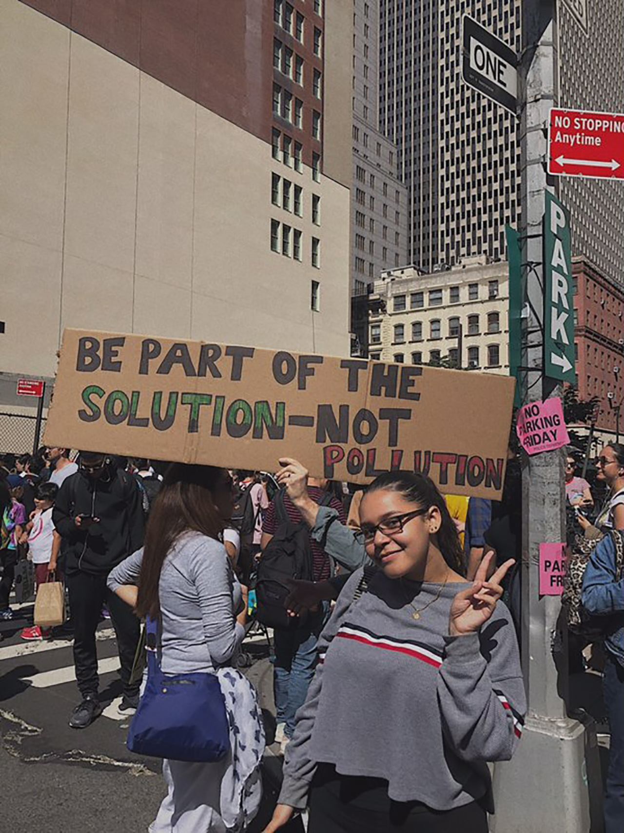 Alexia Leclercq offering a peace sign in front of a “Be part of the solution—not pollution