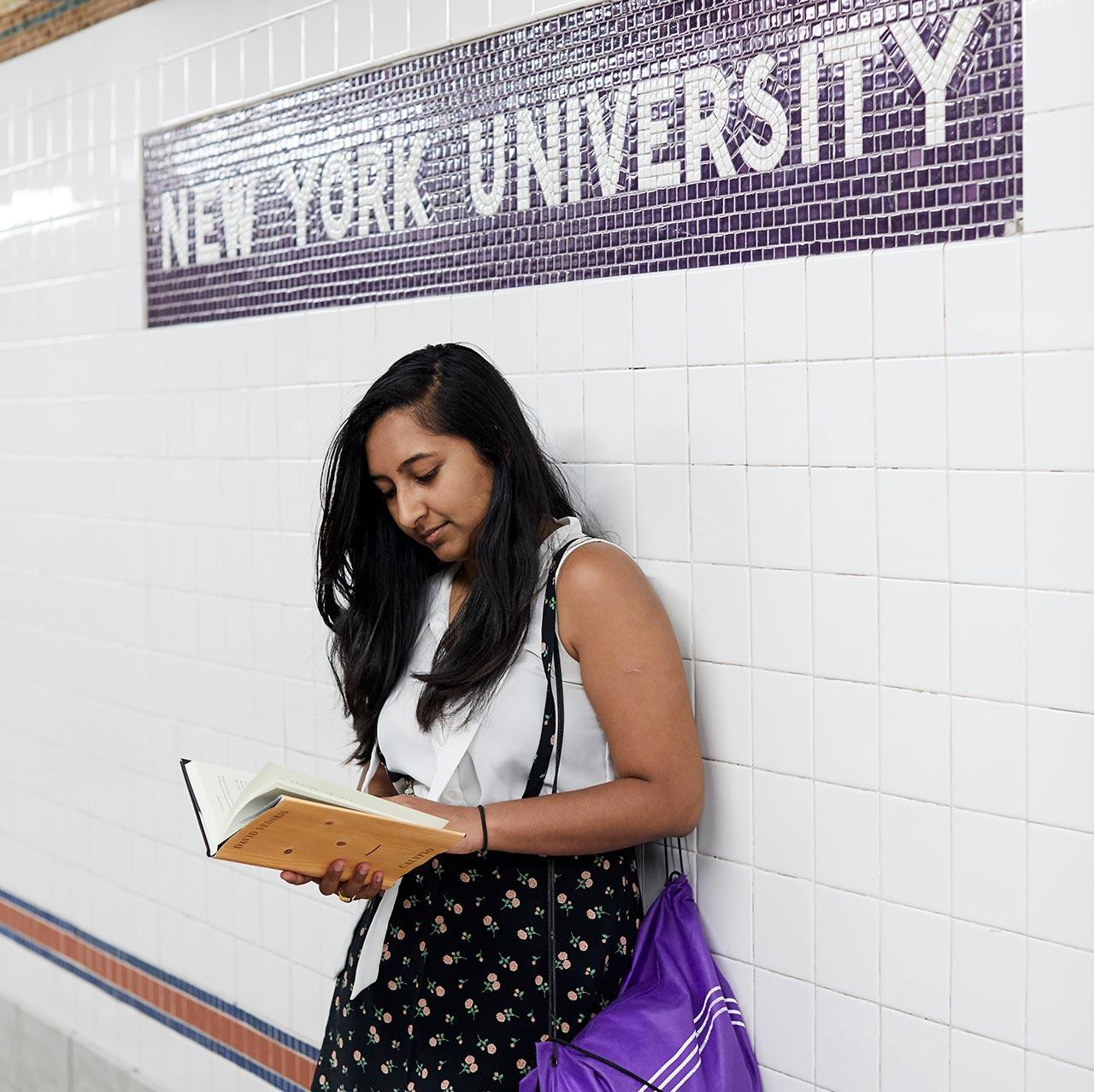 NYU student reading a book on a subway platform.