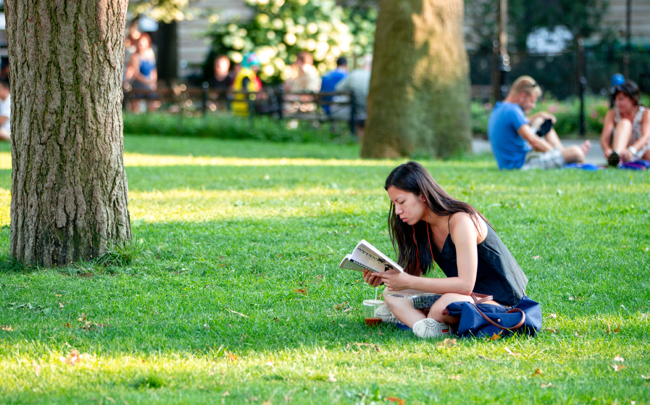 A student reading a book on the grass in Washington Square Park.