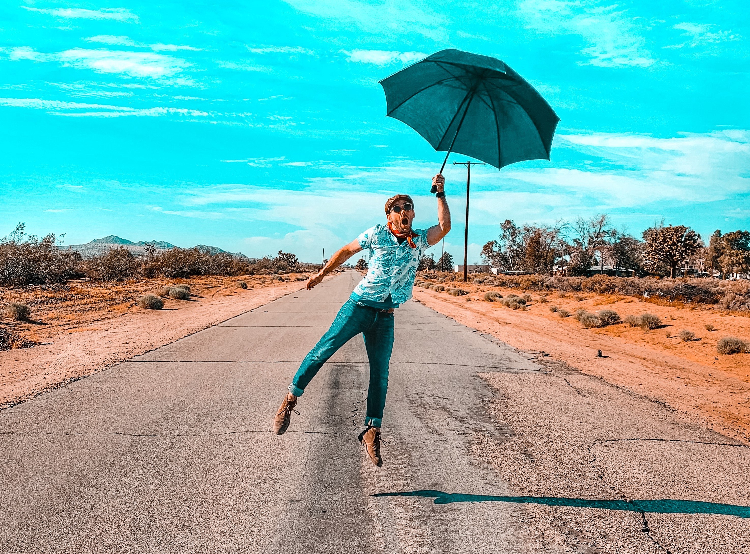 A happy man holding an umbrella and jumping in the middle of a road.