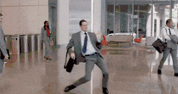 A man in a suit dancing around with his briefcase in an airport.