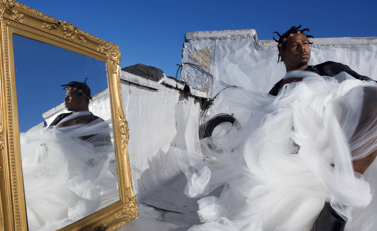 Mark West on a rooftop in NYC posing for a picture. A mirror placed to the left of him shows his reflection