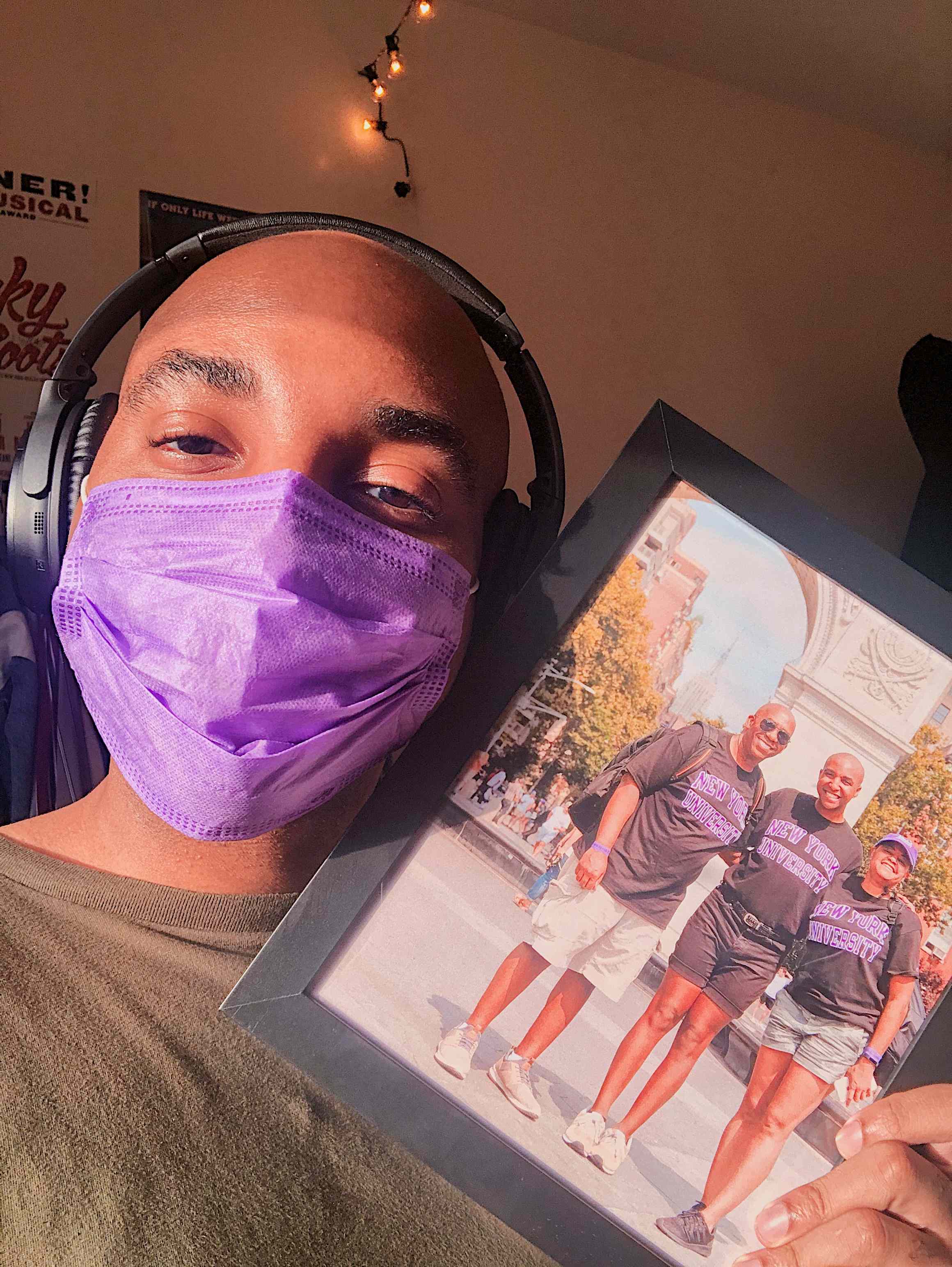 Student holding up a framed photograph of his family while wearing a mask.