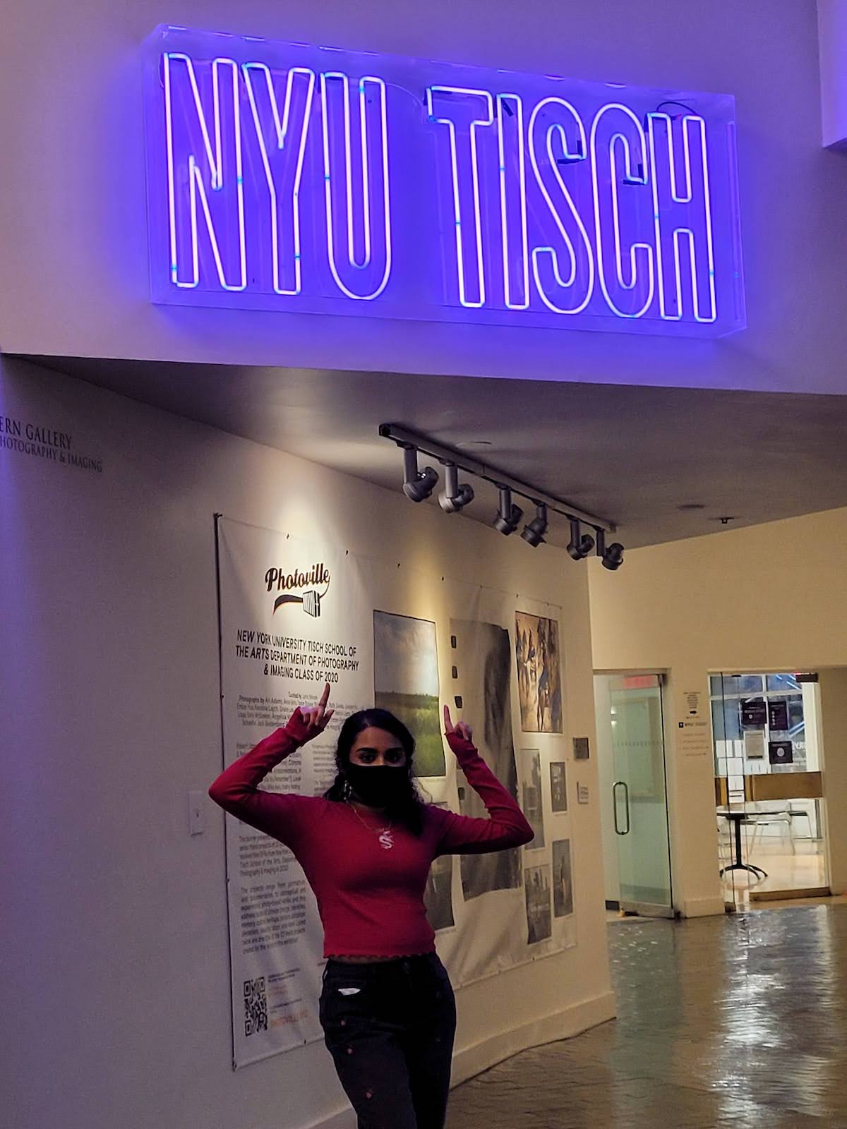 Eshika at NYU Tisch pointing to the Tisch sign.