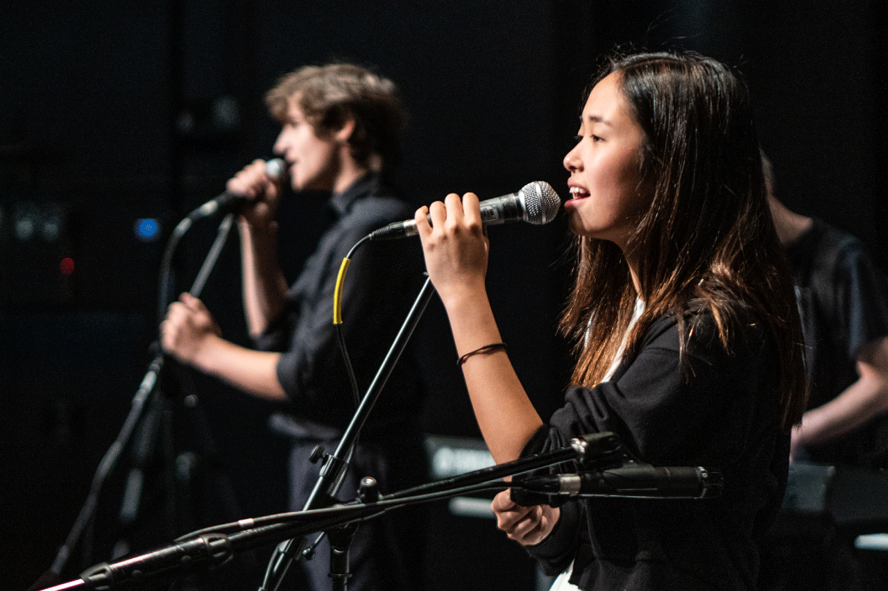 Two students singing into microphones onstage.