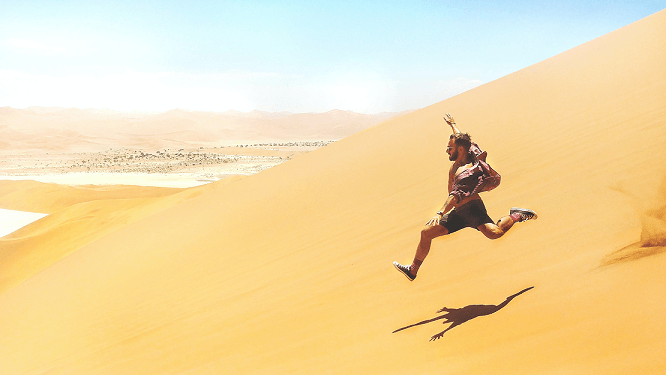 A person jumping on a sand dune.