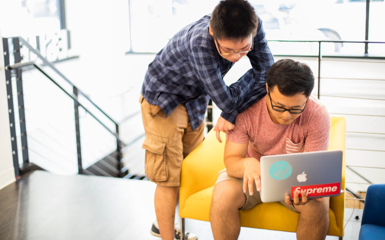 A student working on his laptop while another student looks over his shoulder.