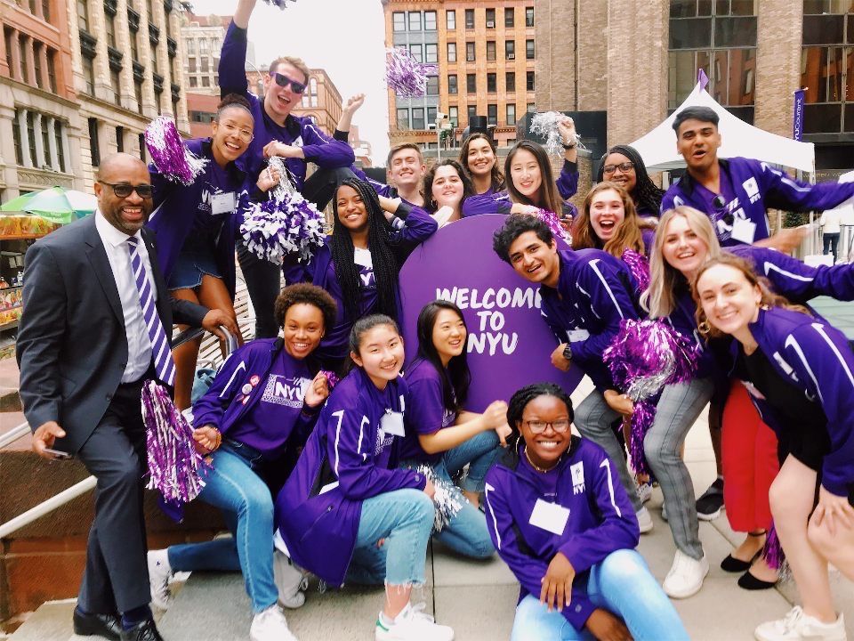 A group of NYU students smiling in front of a “Welcome to NYU” sign.