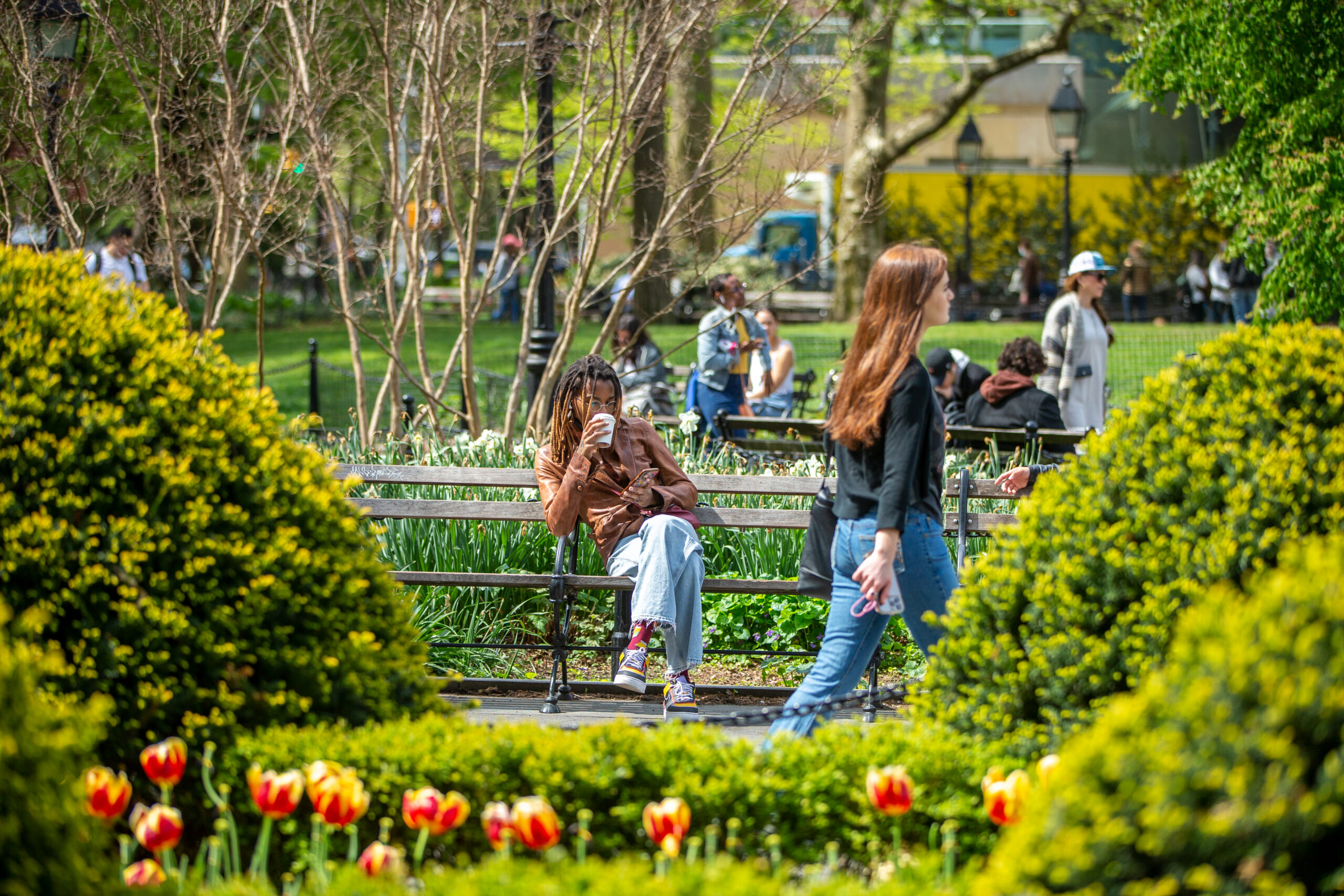 A student sitting on a bench in Washington Square Park drinking a coffee.