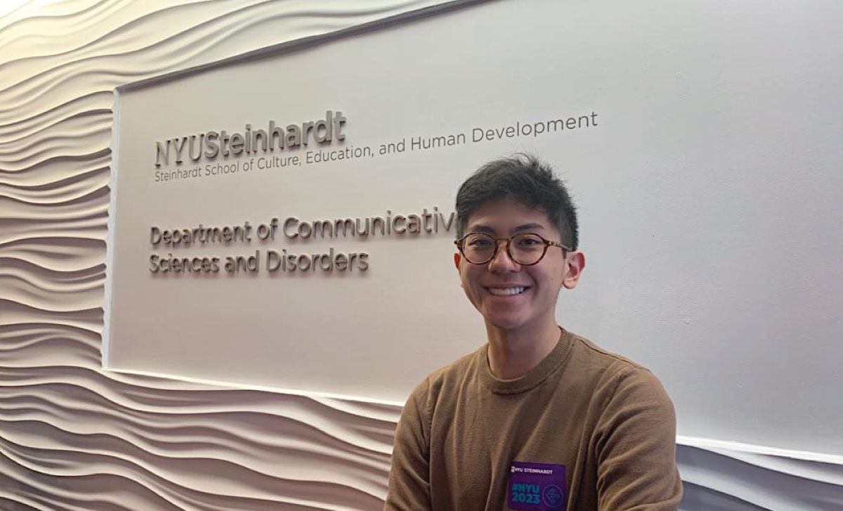 Kenzo Kimura standing in front of a sign for the Department of Communicative Sciences and Disorders.