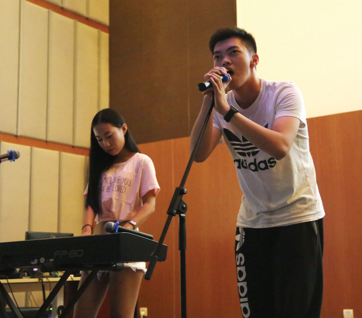 A student singing on stage, while another student plays an instrument
