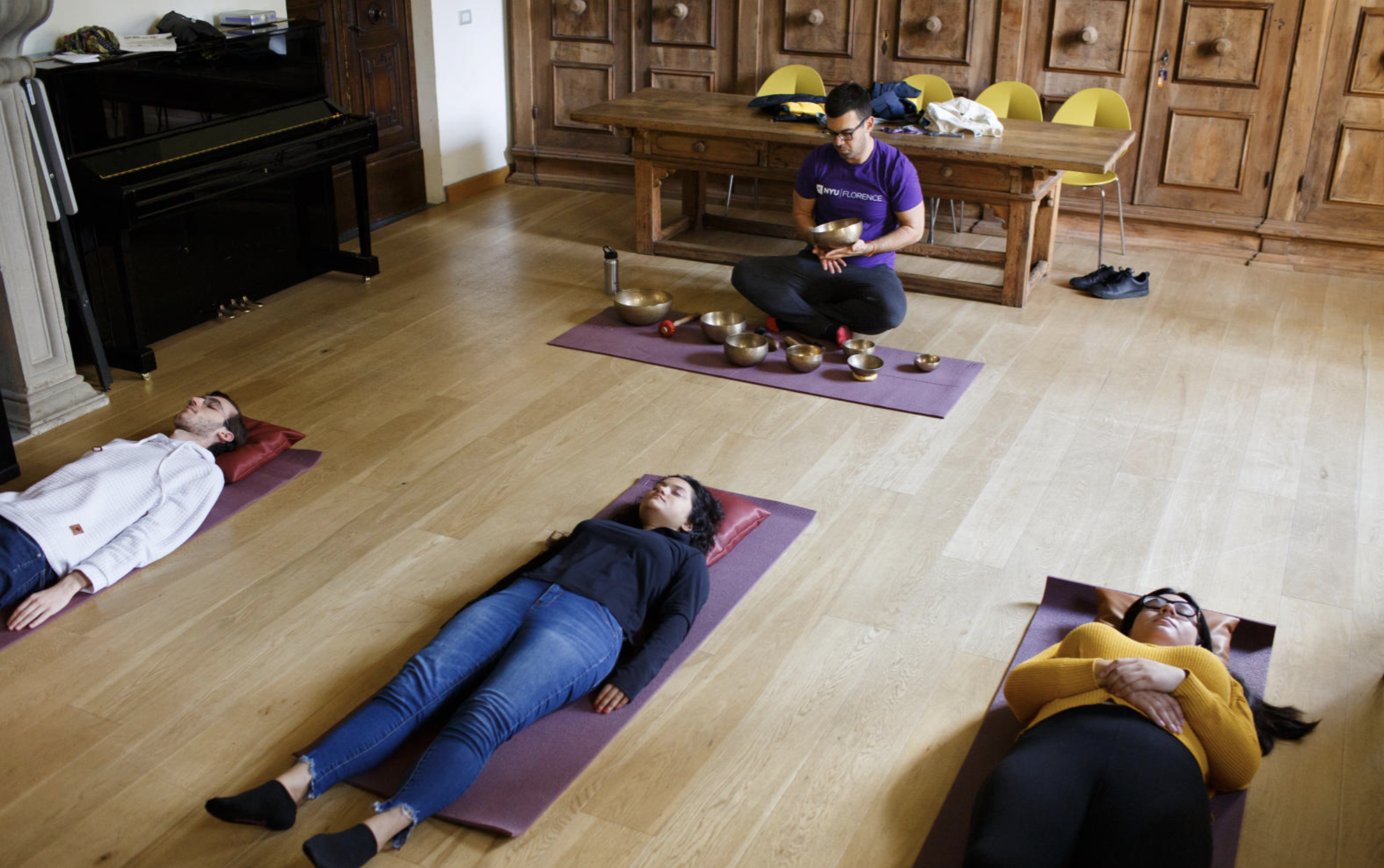 Students lay down on yoga mats while the instructor plays a singing bowl.
