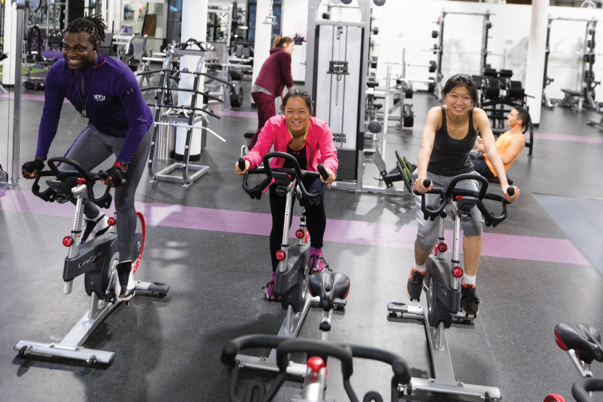 Three students using stationary bikes in the gym.