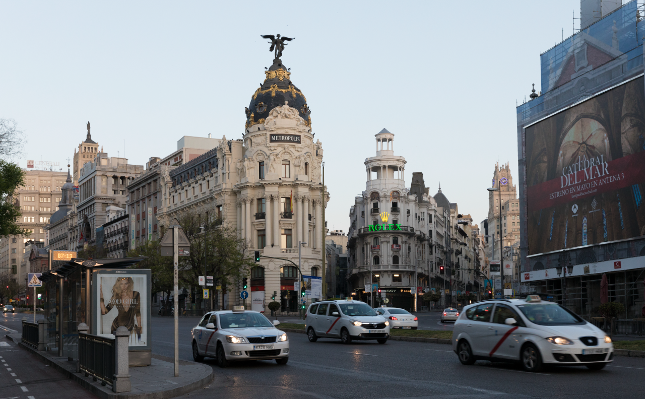 A busy Madrid street corner with traffic at dusk.