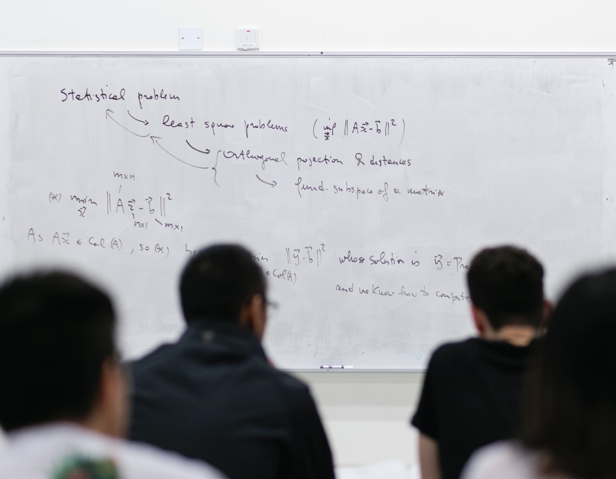 A group of students in front of a whiteboard with equations on it.