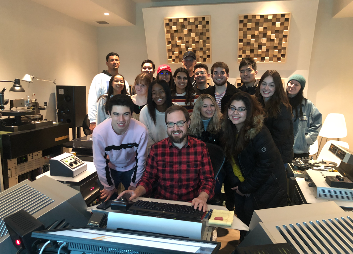 A group of students huddled around equipment in a recording studio