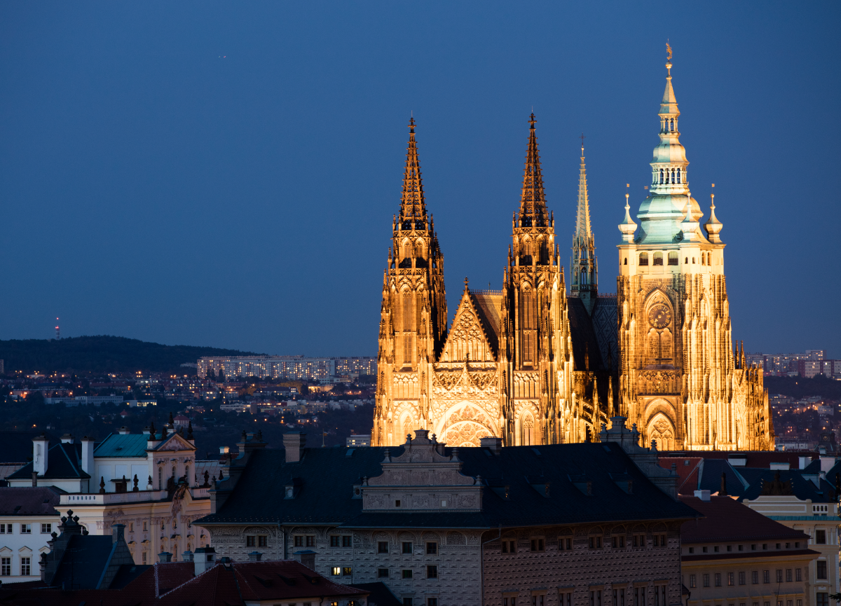 The skyline of Prague at nighttime, featuring a brightly illuminated church.