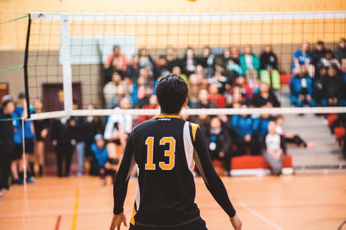 The back of a volleyball player and a volleyball net with a game crowd in the background.
