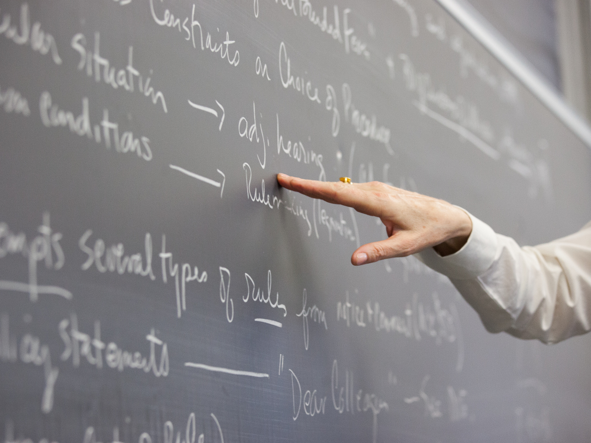 A professor pointing to written notes on a chalkboard.