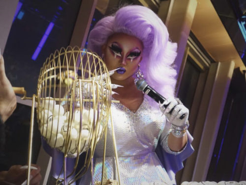Drag Queen standing with a microphone and a bingo game