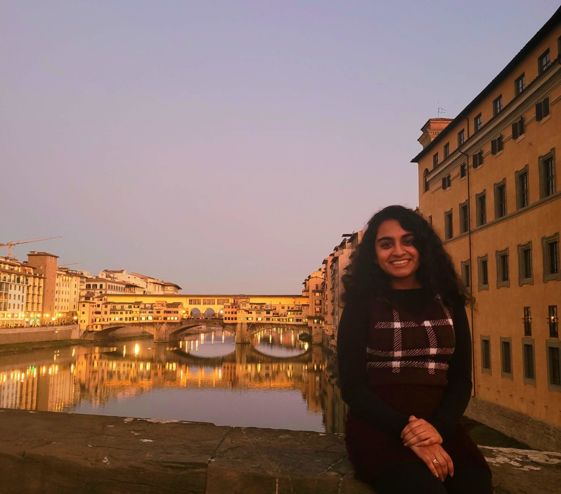 Eshika smiling in front of the Ponte Vecchio at sunset.