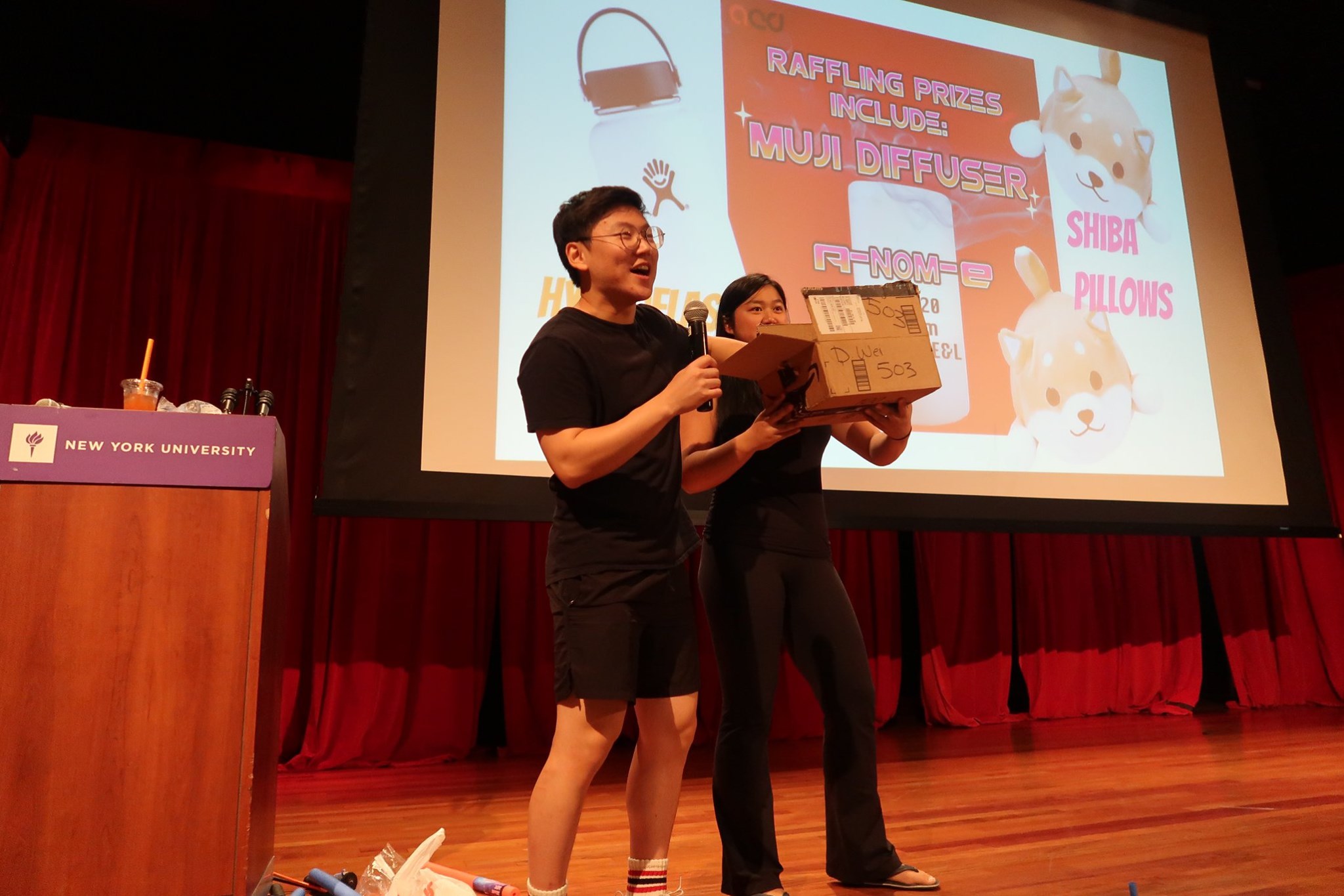 Two students on stage, drawing raffle tickets for prizes.