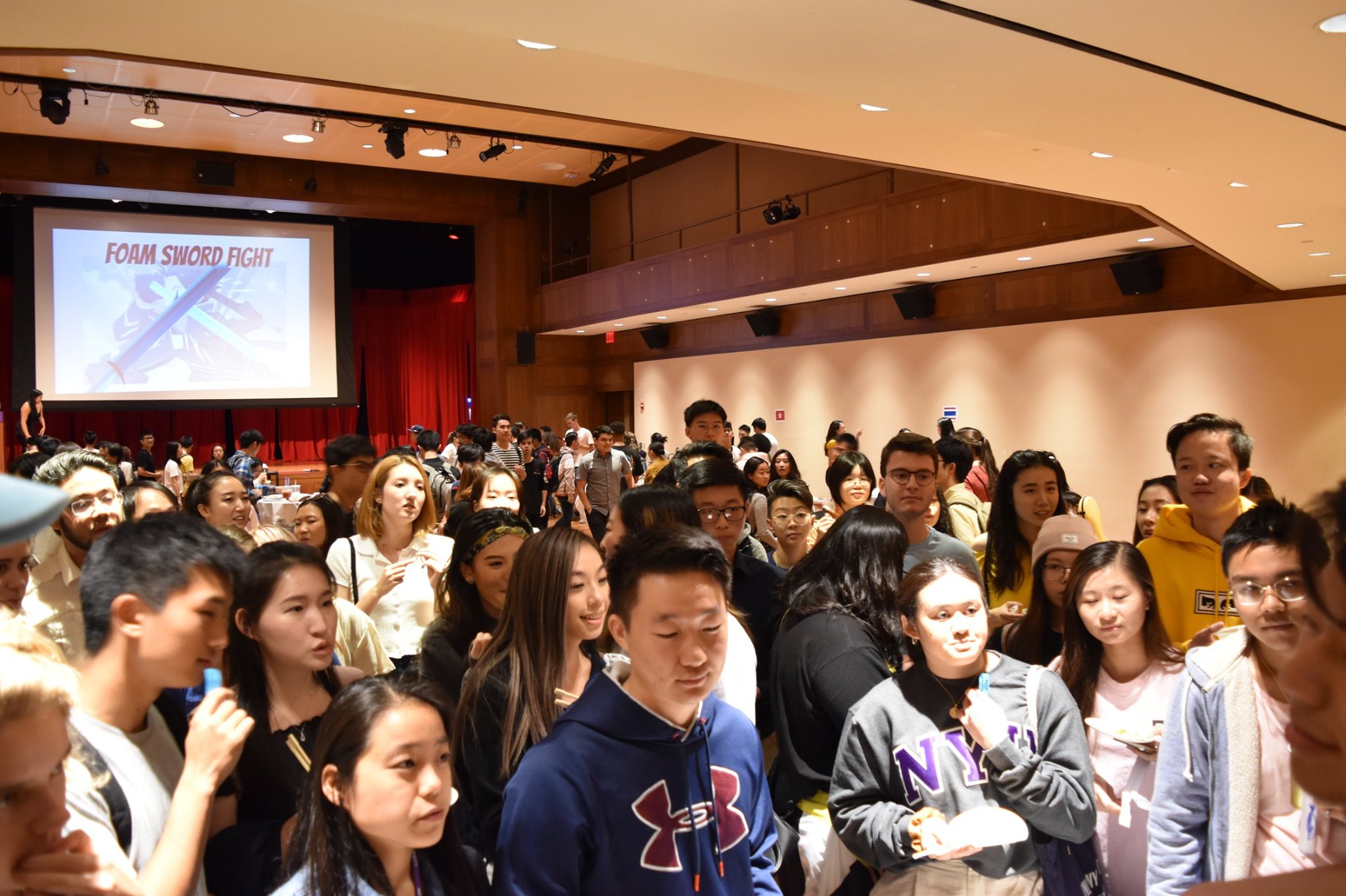 A large group of students socializing in a packed auditorium.