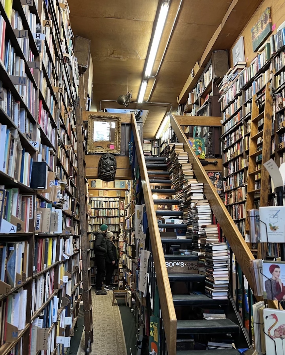 A staircase with books stacked to the side leads to an upper floor of Westsider Rare and Used Books Inc.