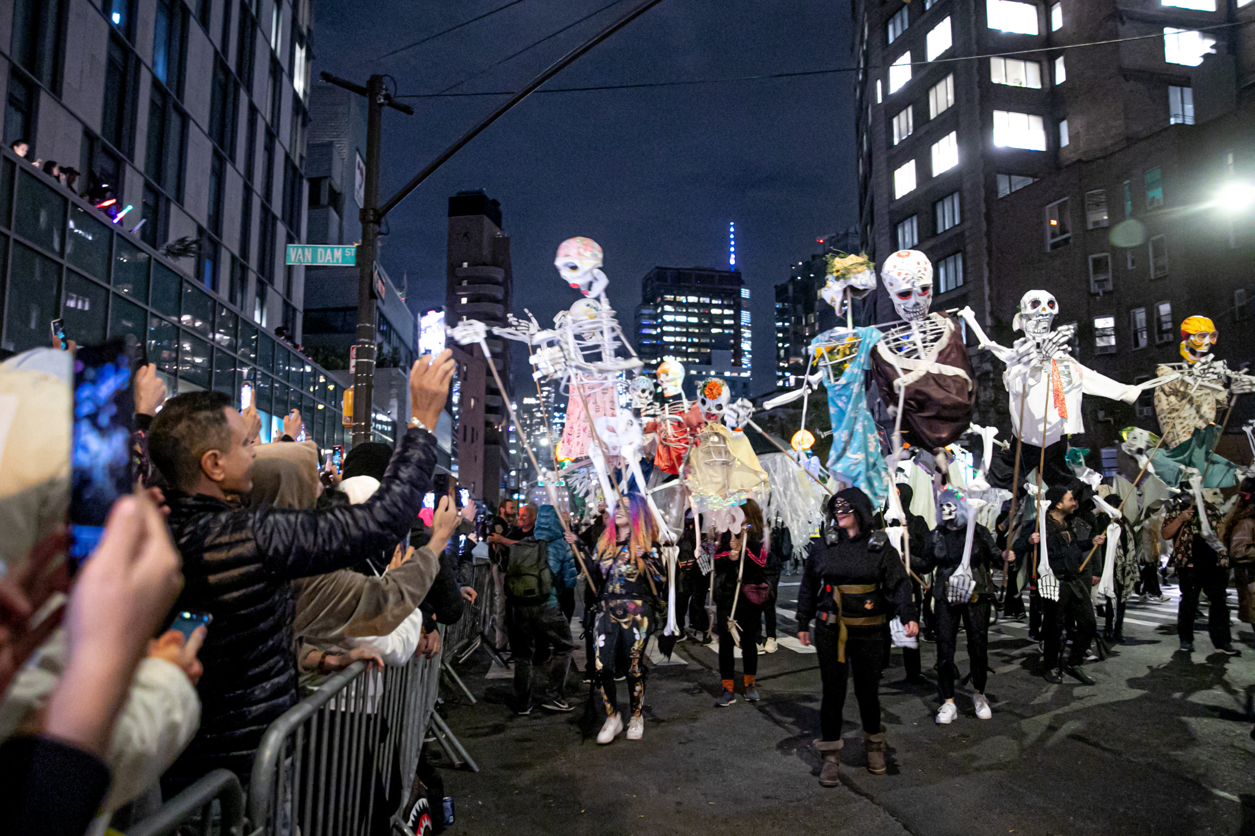 A crowd watches skeleton puppets go by in a Halloween parade.