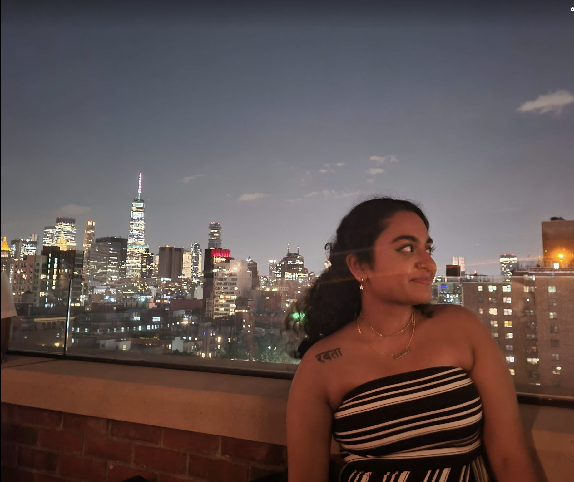 Student standing on a New York City rooftop with the skyline light up behind her at night.