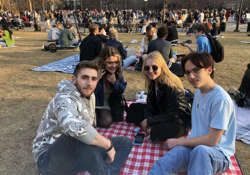 Four European Society students smiling while sitting on a picnic blanket in a park.