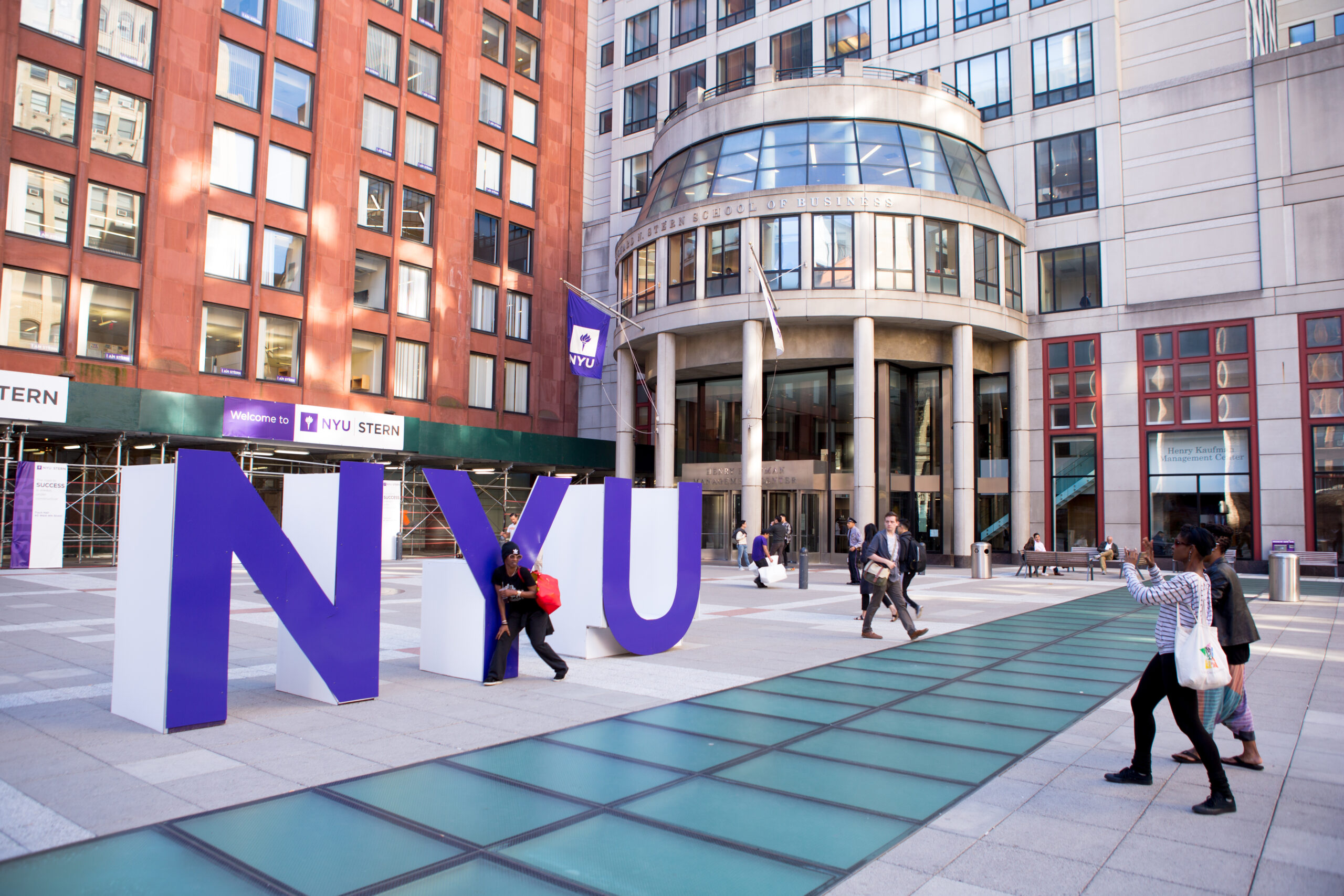 A student of color taking photos next to large sculptural letters that spell “NYU.”