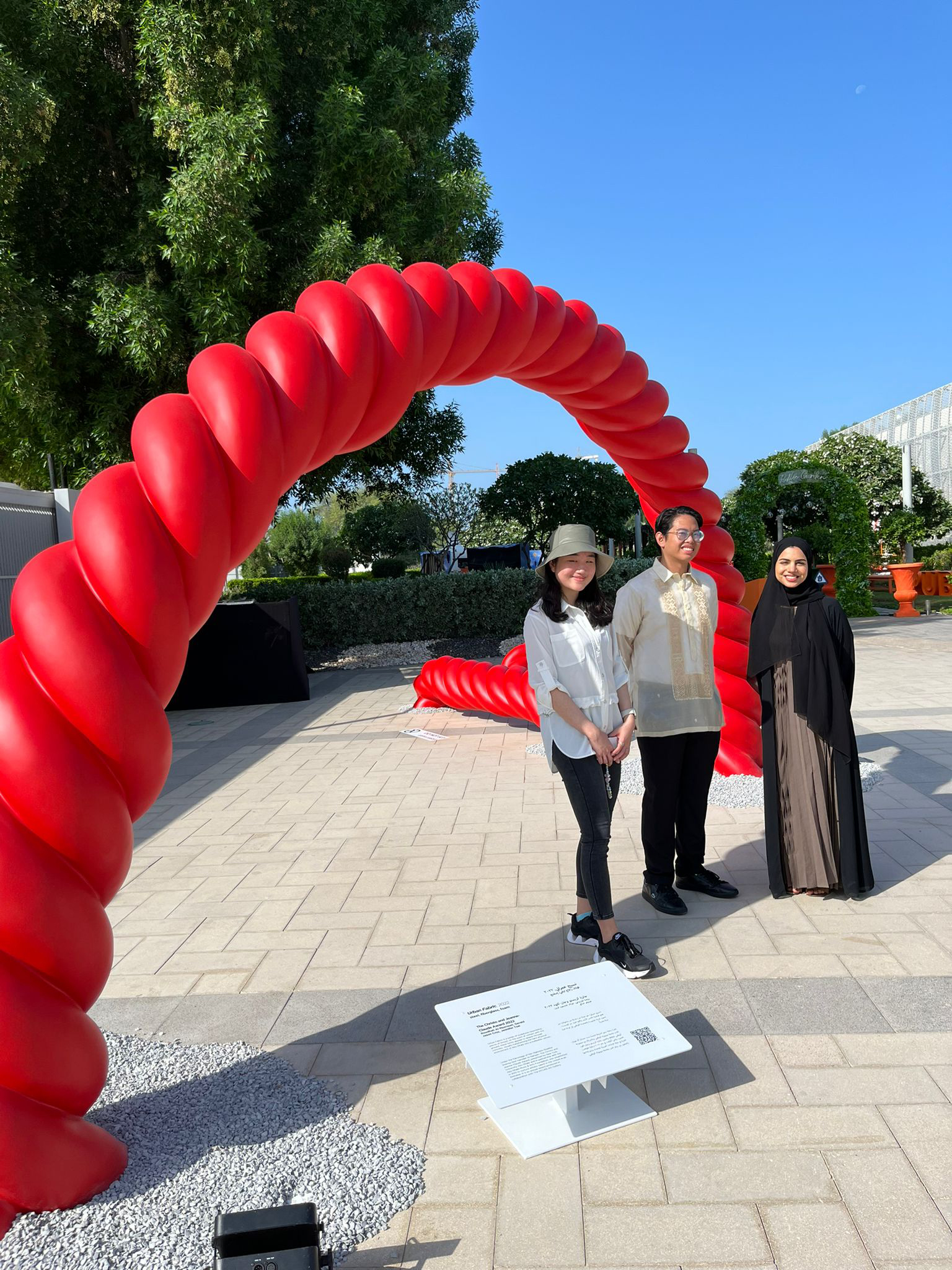 Students in front of their winning installation, “Urban Fabric.” The work is a large red braid-like sculpture curved into an arch.