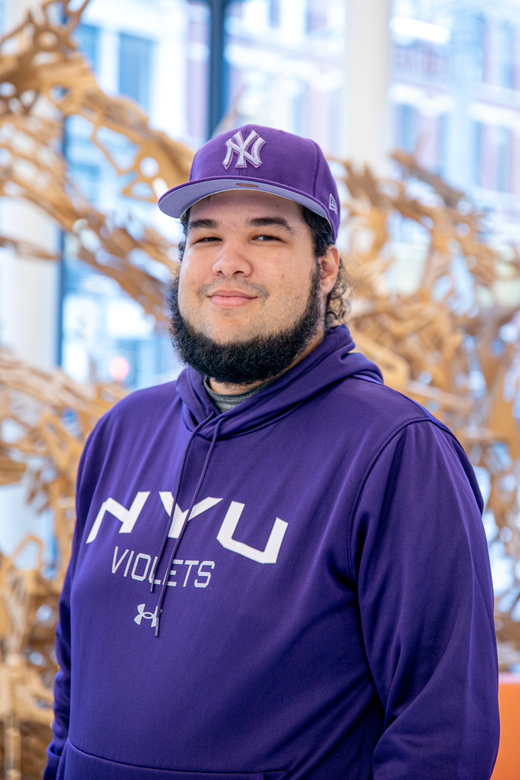 CCTOP scholar Freddy Sanchez wearing an NYU Violet sweatshirt and purple Yankees baseball cap.