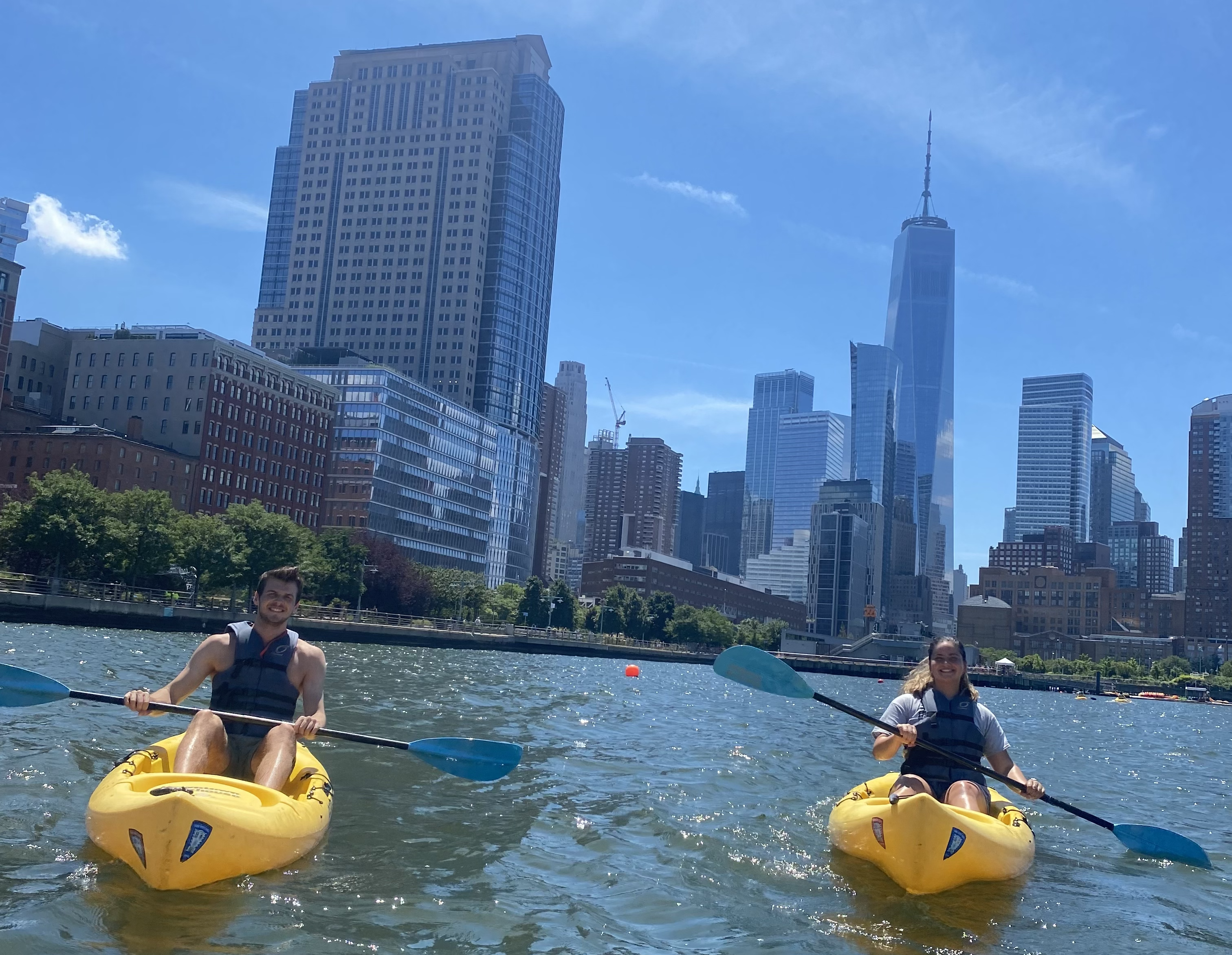 Two students kayak in a river in front of the NYC skyline