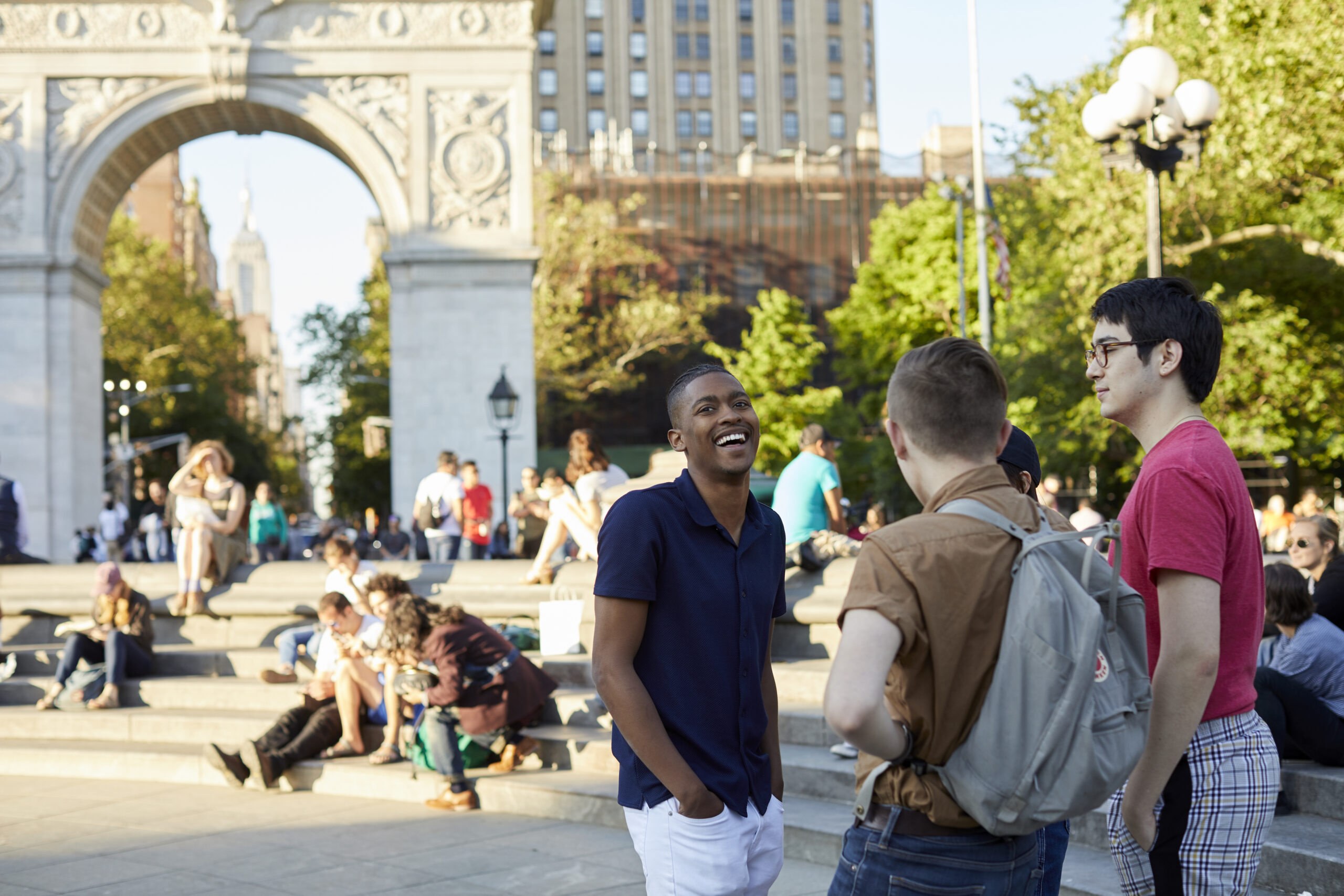 A student of color laughs with his hands in his pockets while congregating with peers in Washington Square Park.