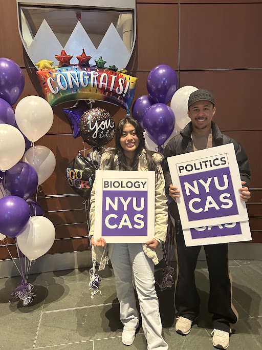 Two CAS students holding signs with their declared majors, Biology and Politics, on them with violet and white balloons in the background.