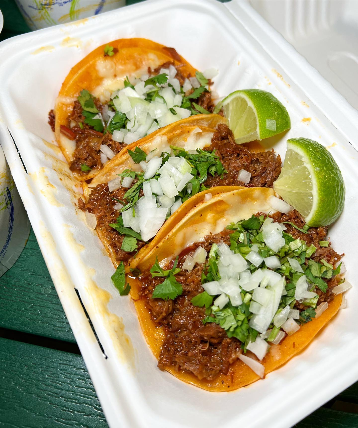 Three Birria tacos in a white to-go box.