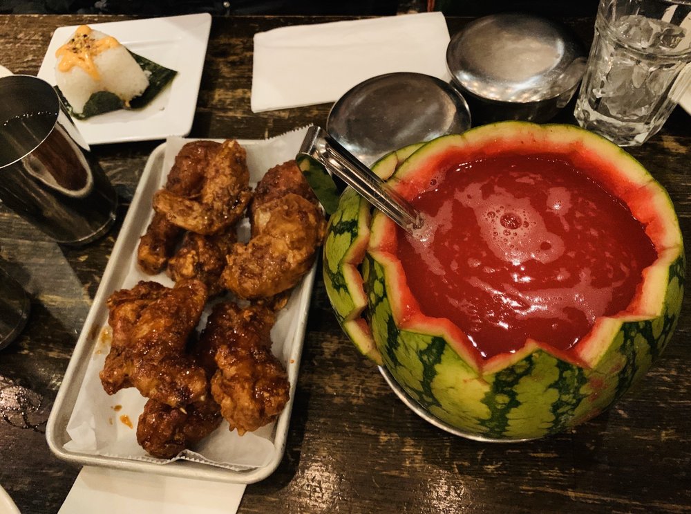 Korean fried chicken on a table next to a hollowed-out watermelon holding juice.