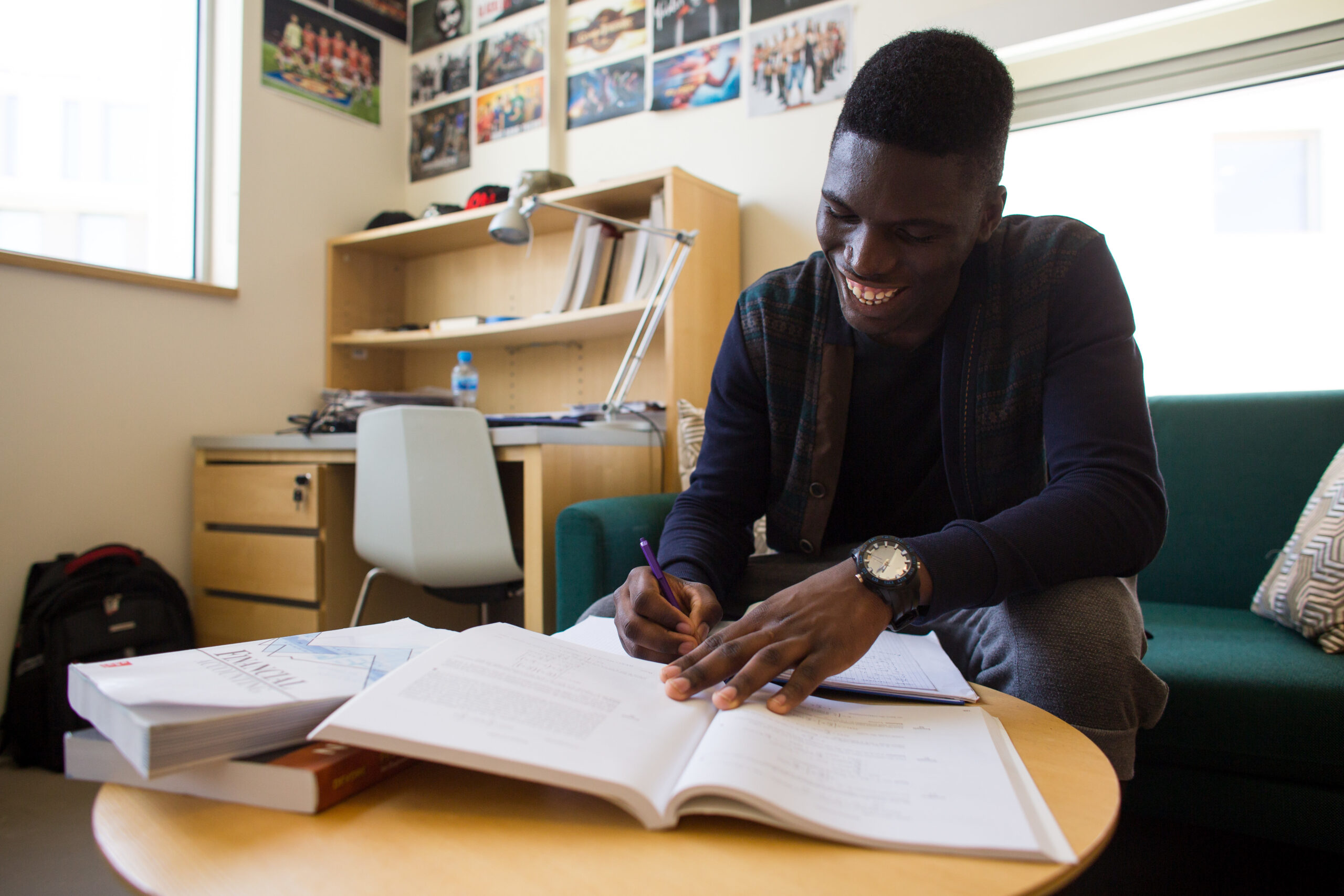 A Black male student writes in a notebook in a dorm room.