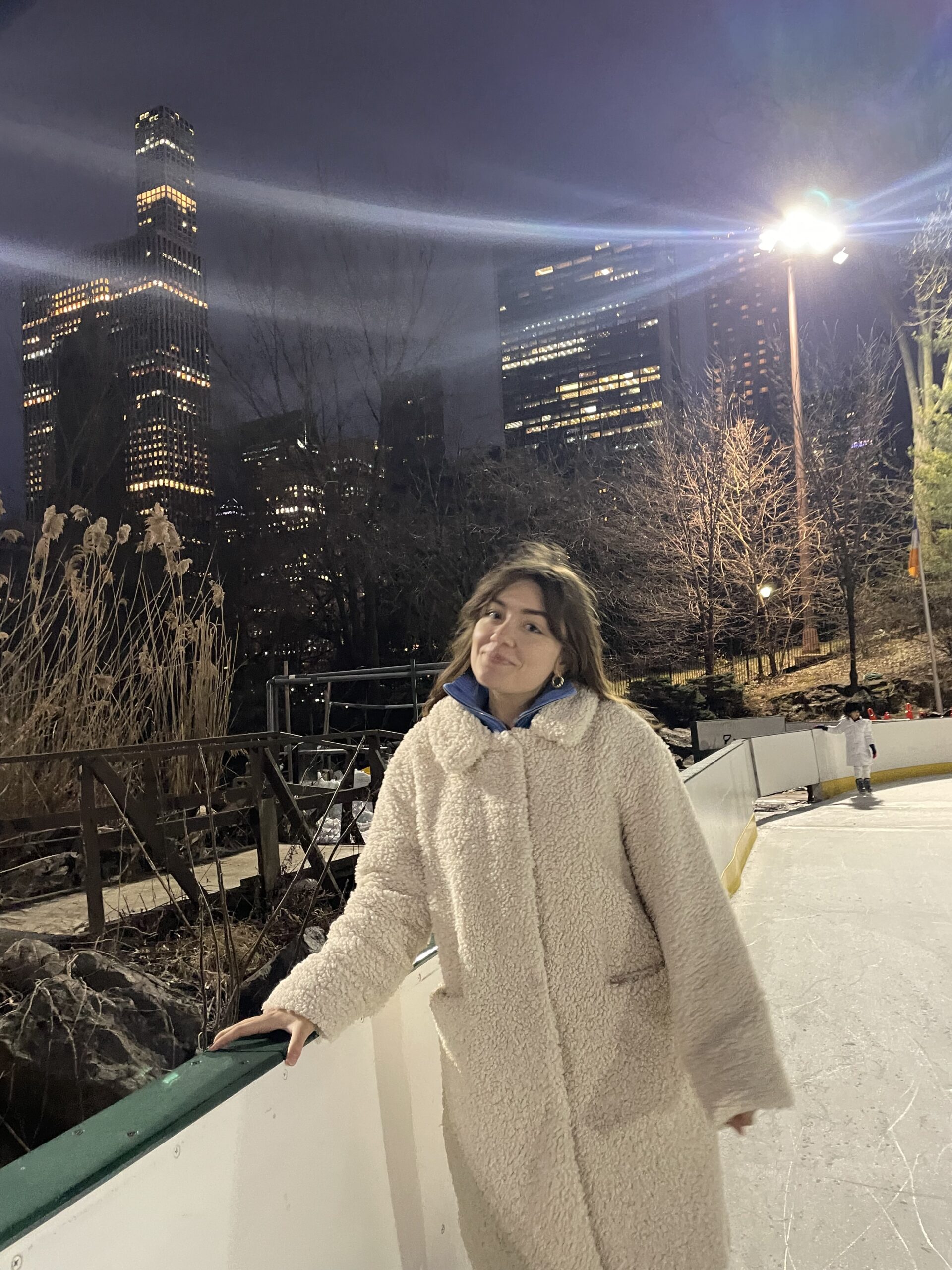 Amina smiles in front of a NYC skyline at Wollman rink