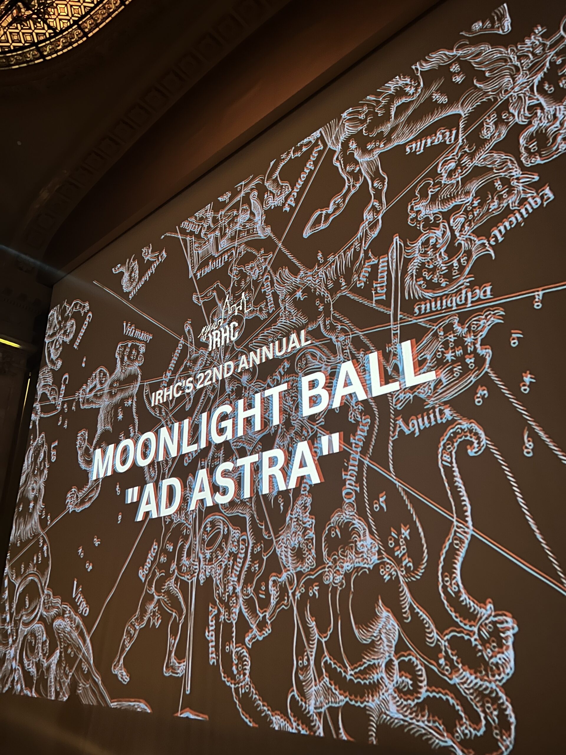 A projection screen reads, “IRHC’s 22nd Annual Moonlight Ball ‘Ad Astra.’”
