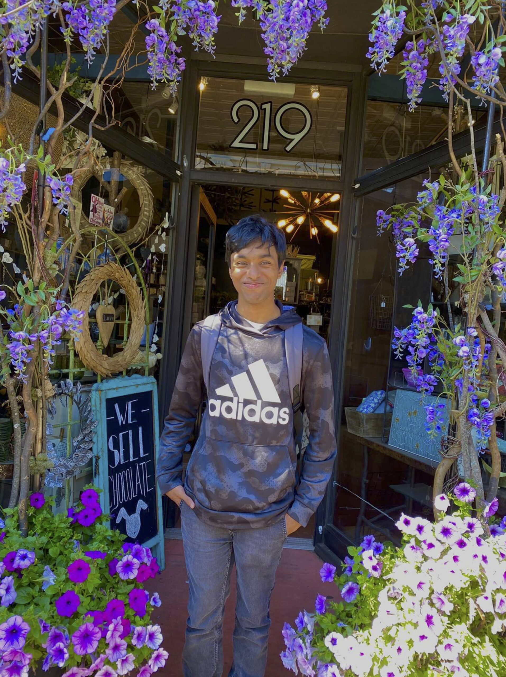 NYU student Armaan Gupta stands in front of a flower-filled storefront that sells chocolates.