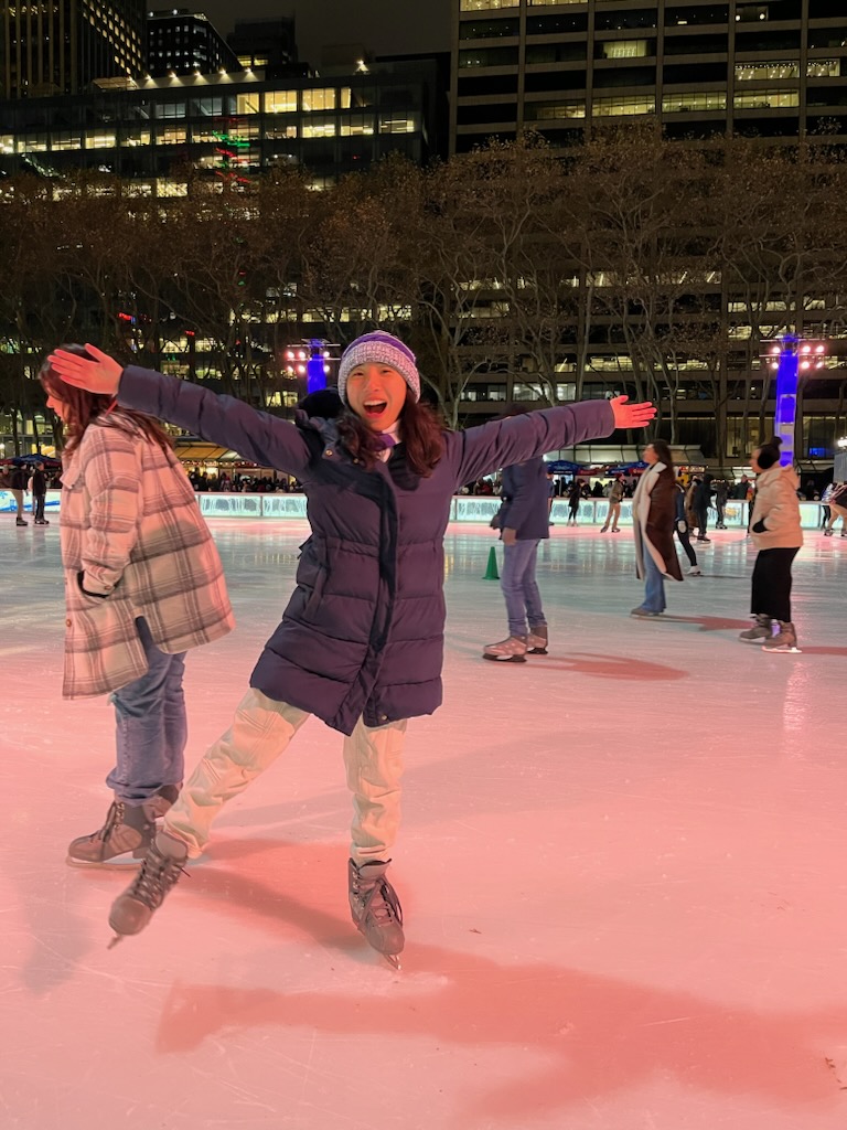 An NYU student ice-skating with their arms extended wide.